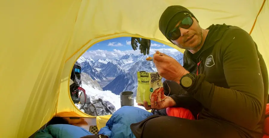 horolezec sedí ve stanu vysoko v horách a jí vakouvě sušené jídlo adventure menu ze sáčku