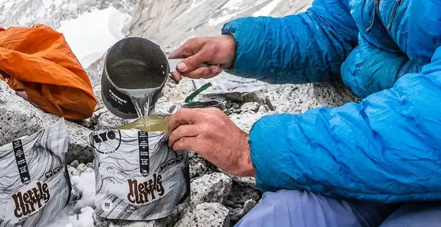 muž v zimních horách zalévá sáček s dehydrovaným jídlem studenou vodou