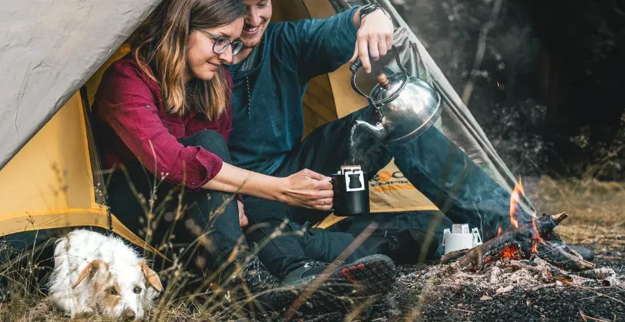 pár sedí v přírodě před stanem a připravuje si kávu ve filtru dripit