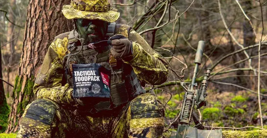 voják v maskáčích sedí v lese a jí jídlo tactical foodpack přímo ze sáčku