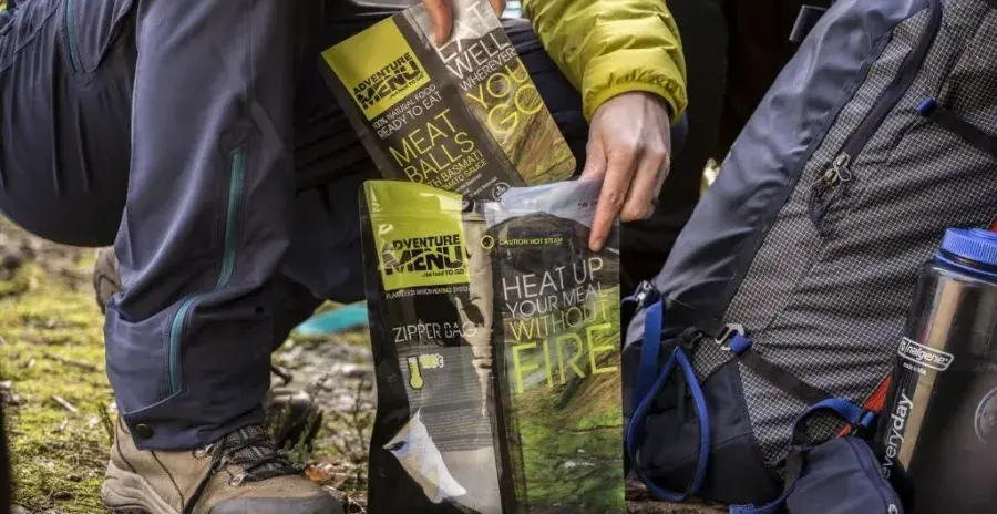 muž v podřepu umisťuje sáček s hotovým MRE jídlem do samoohřevného sáčku Zipper bag od adventure menu