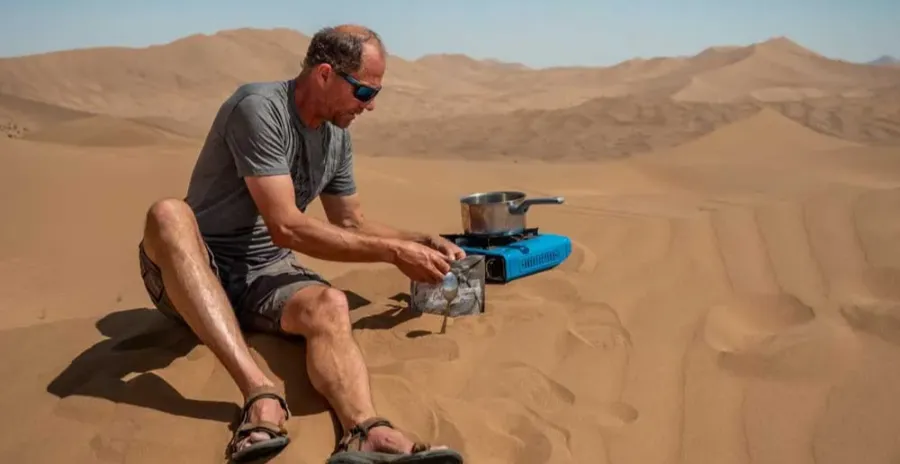muž sedí na poušti a připravuje si dehydrované jídlo