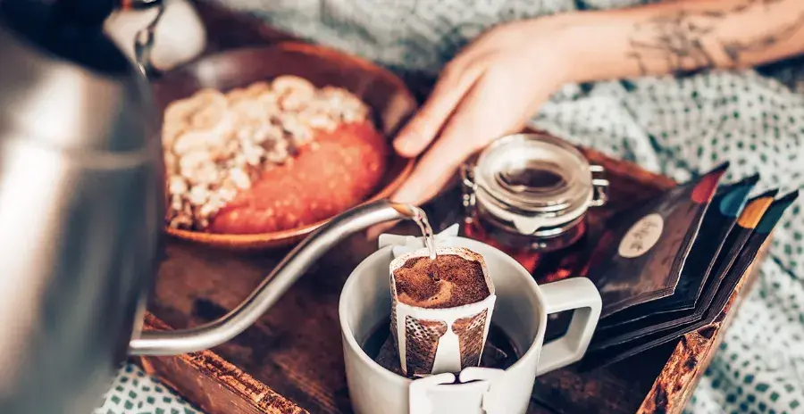 žena leží v posteli a má u sebe snídani s kávou připravenou z filtru dripit