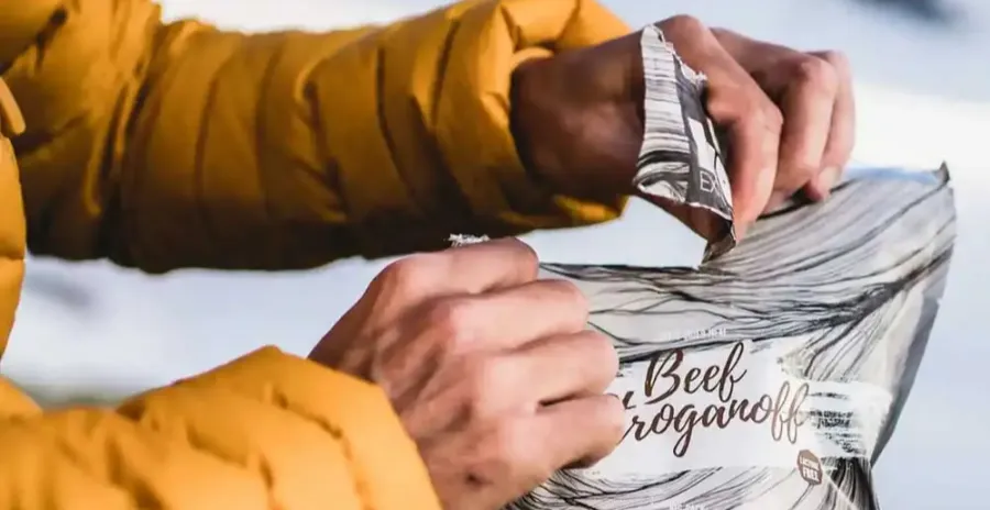 muž na sněhu otevírá sáček s lyofilizovaným jídlem lyofood