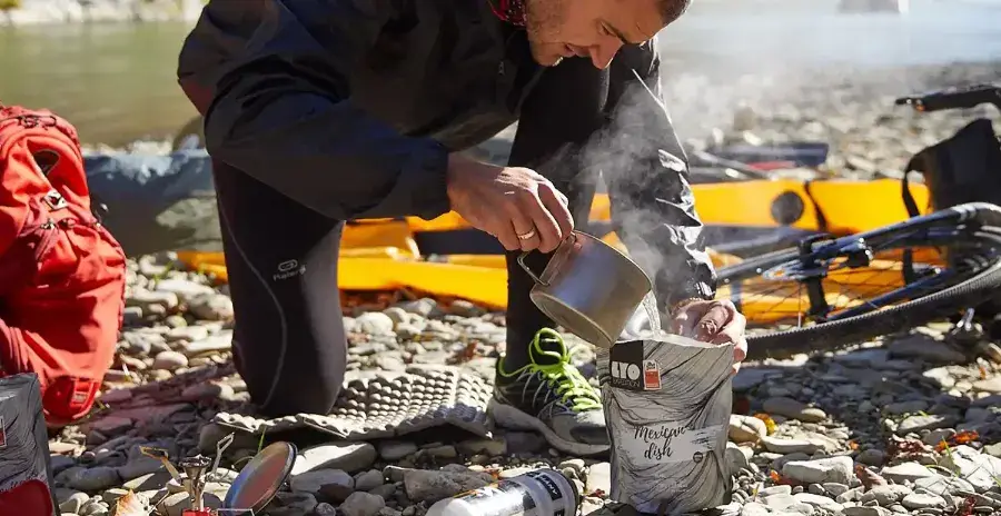 cyklista u řeky nalévá vodu do sáčku s lyofilizovanou snídaní