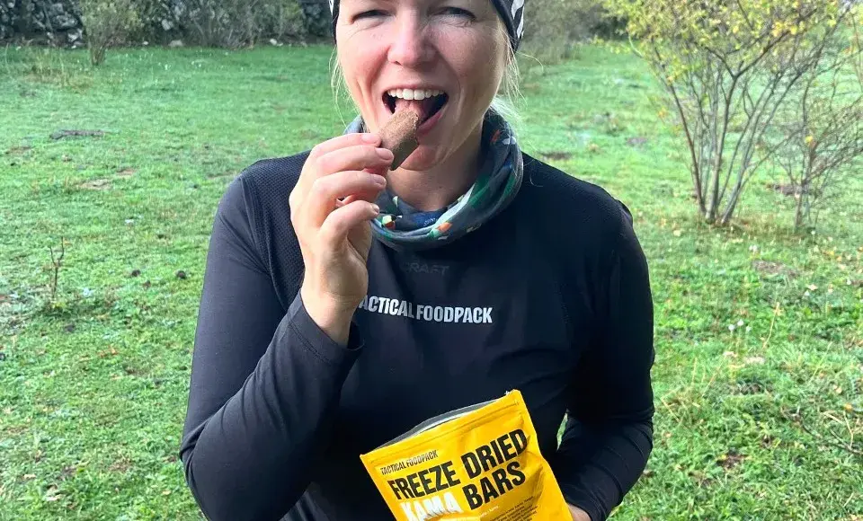 žena stojí na louce a jí mrazem sušený dezert od Tactical Foodpack, který je připraven k okamžité konzumaci