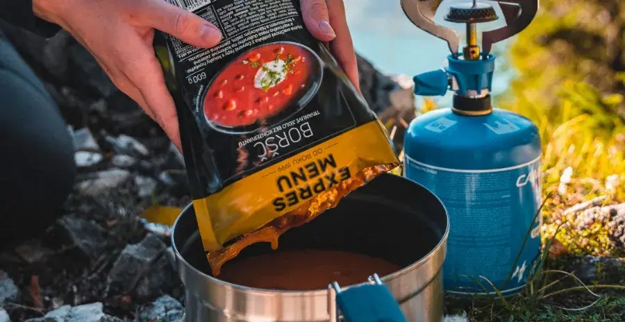 muž v kempu vylévá obsah sáčku s hotovu mre polévkou expres menu do hrnce