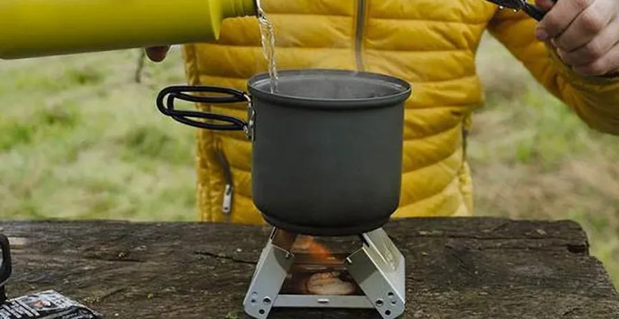 muž v přírodě ohřívá polévku na vařiči na tuhá paliva