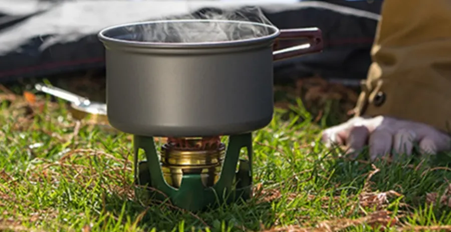 muž na trávě vaří jídlo na lihovém vařiči