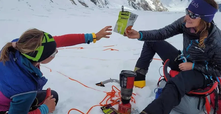 lezkyně na sněhu v horách podává sáček s lyofilizovaným jídlem své přítelkyni