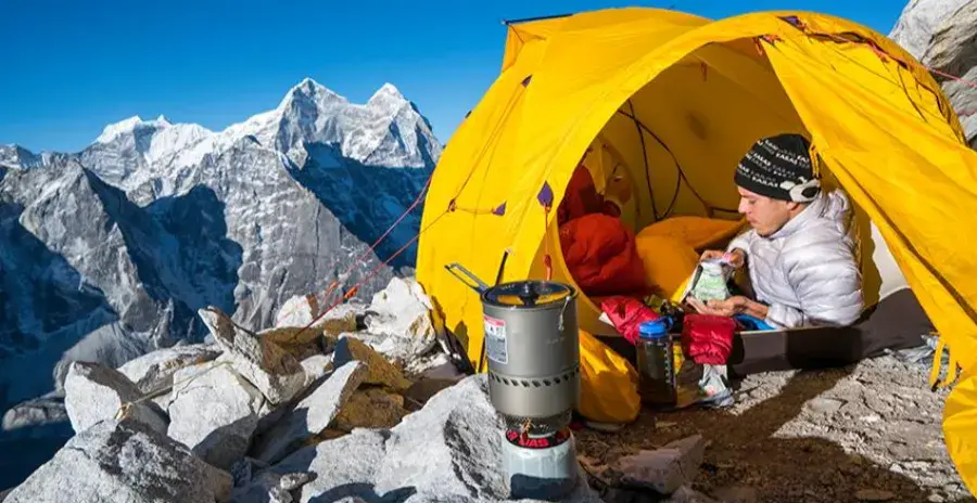 muž vysoko v horách vaří před stanem jídlo na vařiči
