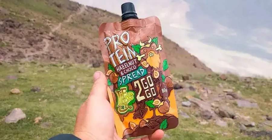 turista natahuje ruku a ukazuje ořechový krém LifeLike 2GOGO v kapsičce s přidaným proteinem