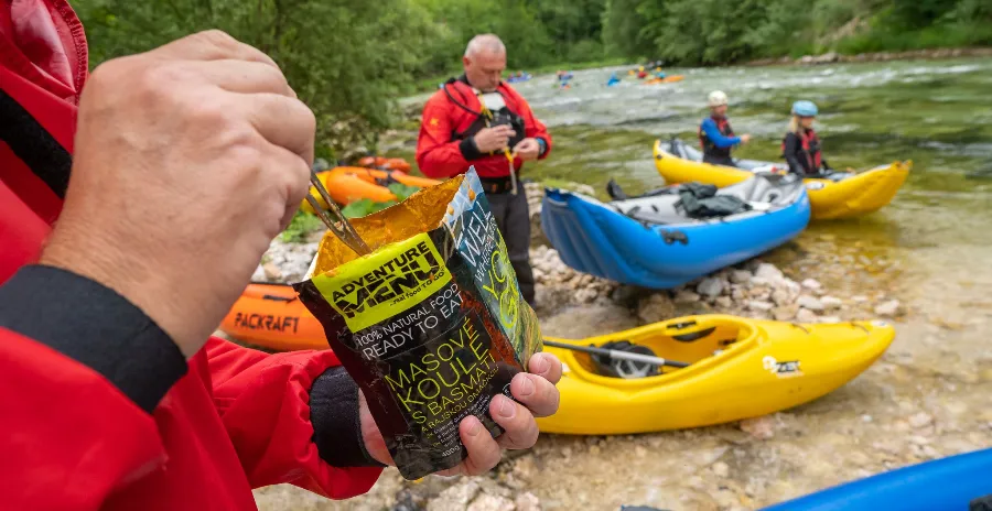 muž stojí na břehu u vody a jí hotový mre hlavní chod přímo ze sáčku