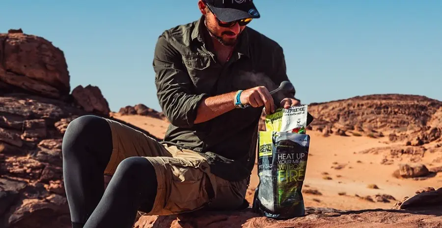 muž sedí na skále a vkládá sáček s lyofilizovaným jídlem adventure menu do zipper bagu