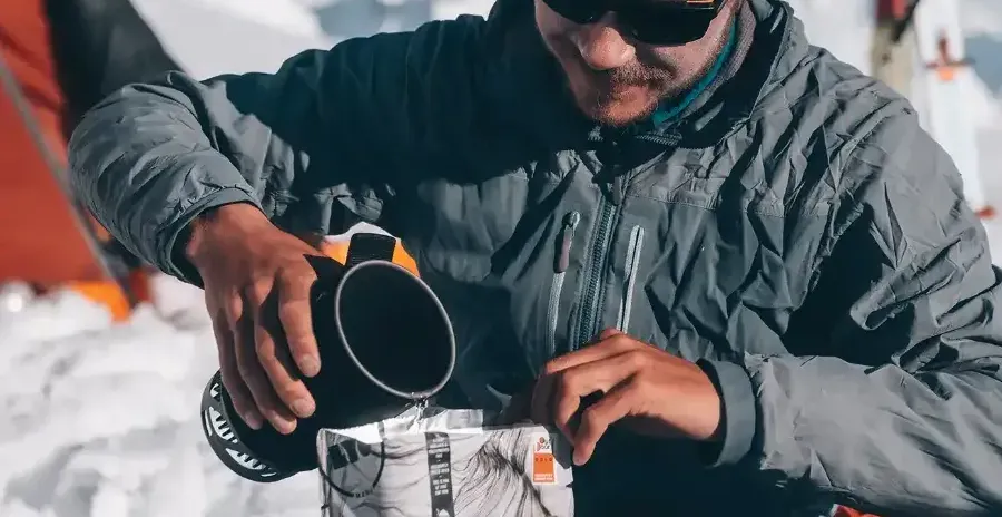 horolezec na sněhu nalévá vodu do sáčku s lyofilizovaným jídlem lyofood