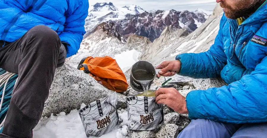 horolezec vysoko v horách zalévá sáček s lyofilizovanou polévkou horkou vodou během expedice