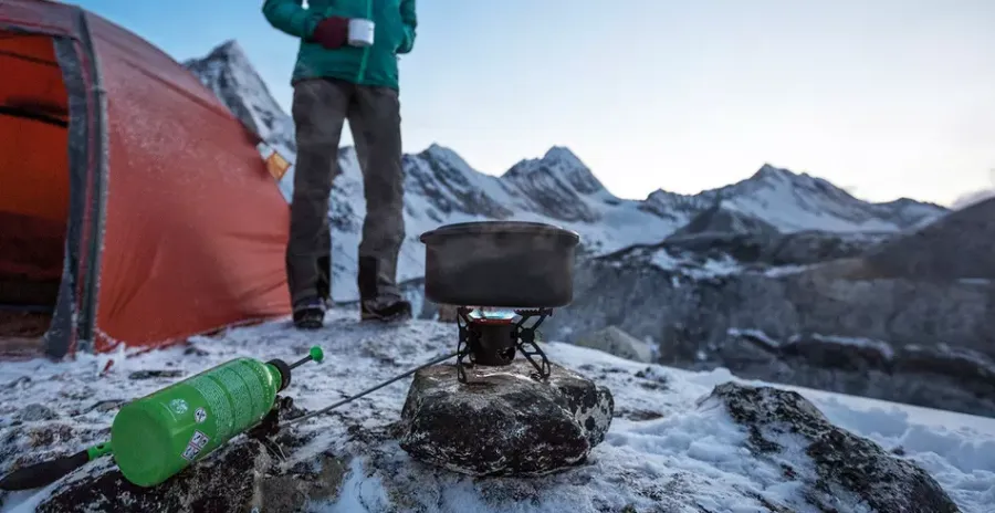 žena v horách u stanu vaří jídlo na benzinovém vařiči