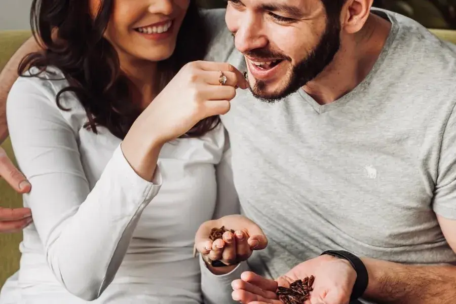 mladá žena sedí na pohovce vedle svého přítele a krmí ho sušeným jedlým hmyzem